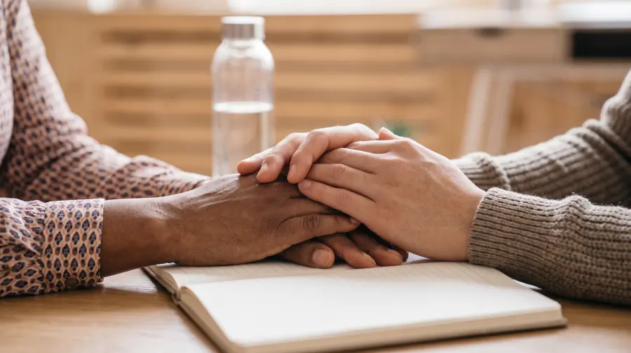 Two people's hands resting together in a gesture of comfort on top of an open notebook